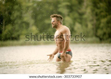 An image of a muscular man in the lake playing with the water