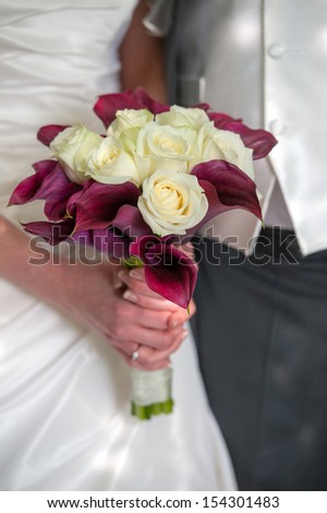 bride holding a wedding bouquet of purple plus white roses and calla lilies