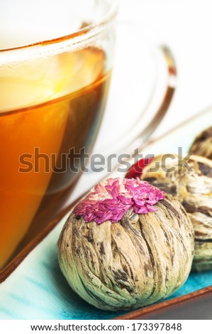 Close-up of flowering tea balls (blooming tea) and cup of tea on white wooden surface