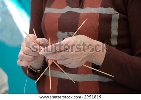 Hands of a mature lady knitting an orange scarf