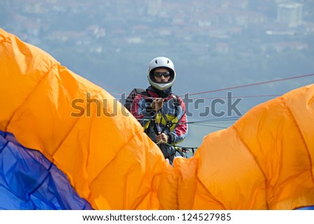 paraglider pilot preparing for lift-off in reverse launch style. Wearing his helmet and gloves, tightly pulls the multi-colored strings, drawn tight by the parachute pulling in the wind