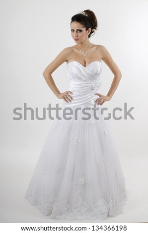 bride posing in white wedding dress holds wedding dress looking forward and standing straight