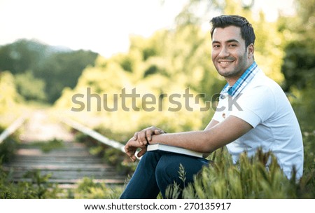 Smile student or man sitting in nature with book, outdoors