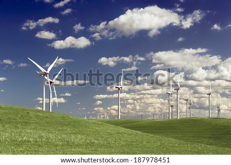 Stark white power generating wind turbines, under Spring blue sky, behind a field of green rangeland, California.