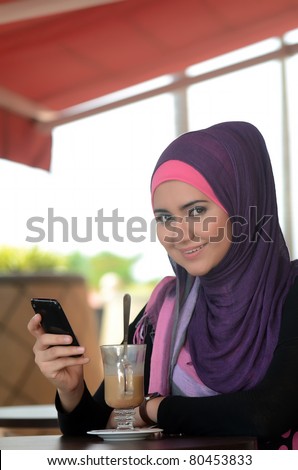 young muslim woman in head scarf using phone in cafe