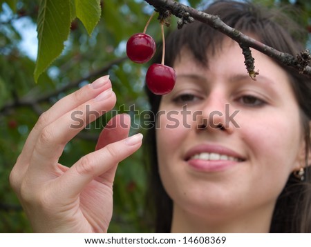 Beautiful young lady picks red cherries from tree