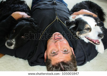 Man\'s best friends.  A man lying on the livingroom carpet hugging his two dogs looks upside down at the camera