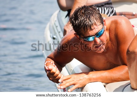 a bronze tanned water ski boat spotter pulling in the rope from the water, in the summer sun