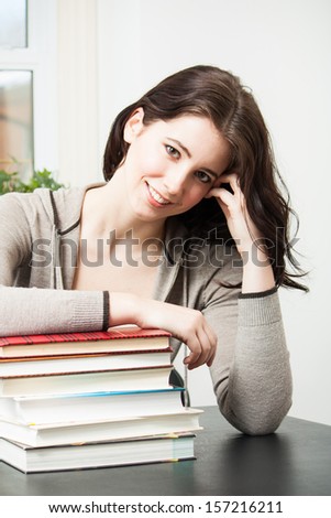 Beautiful brunette college girl smiles at the camera while leaning on a stack of textbooks.  Vertical composition