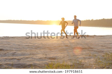 Young man and woman running along the waterfront in sunshine