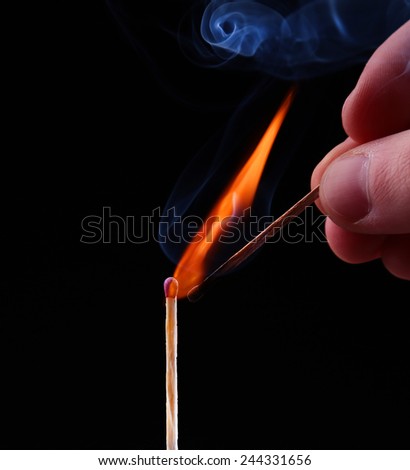 Ignition of a match, with smoke on dark background. Hand holding burning match stick