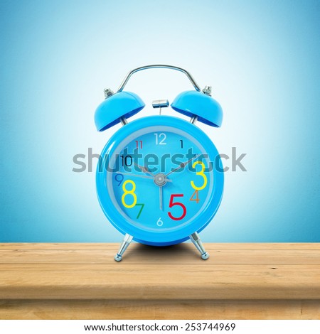 Alarm clock put on the wooden in blue wallpaper room.