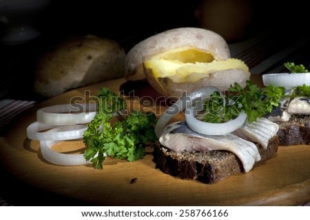 Sandwich made of herring on rye bread, served with onion, jacket potato and parsley