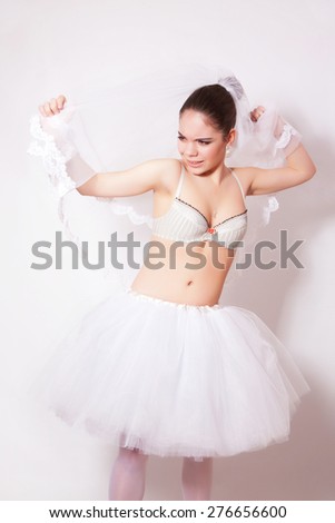 Sad bride in a skirt, underwear and veil on gray background