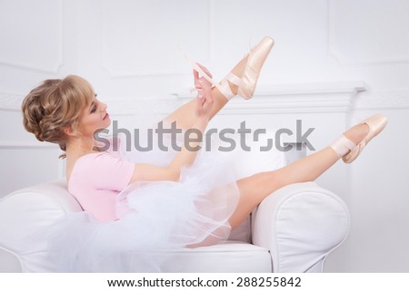 Ballerina tying pointe shoes sitting in a white chair