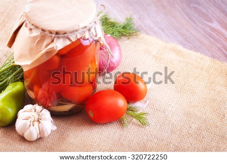 Tomatoes marinated in jars with spices and vegetables on a wooden table