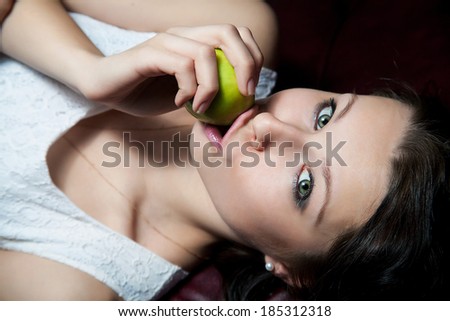 sensual portrait of young woman in white dress sitting on the sofa with an apple