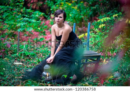 beautiful girl sitting on a chair with lamp and candle in the forest