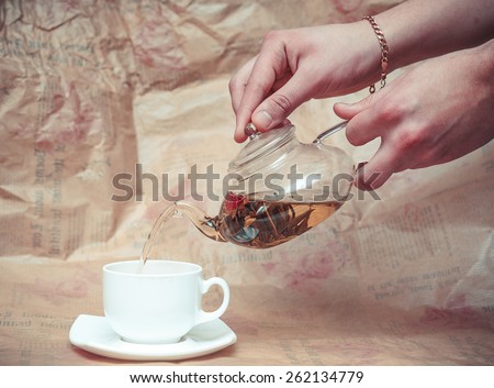 Glass teapot pouring black tea into cup isolated on grey