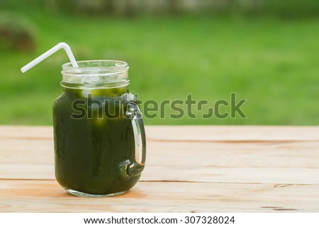 Cube glass with handle of rich cool Centella asiatica juice with white straw on the wooden table in green grass garden