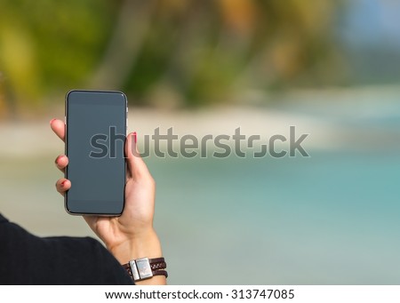 Woman hand showing a blank smart phone on the beach with the sea in the background