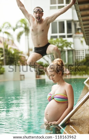 Pregnant woman against her husband jumping into the pool