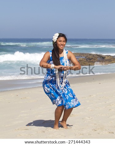 A beautiful teenage girl dancing hula on an empty beach.  She is wearing a traditional hula dance outfit, a long shell necklace and a plumeria flower in her hand.