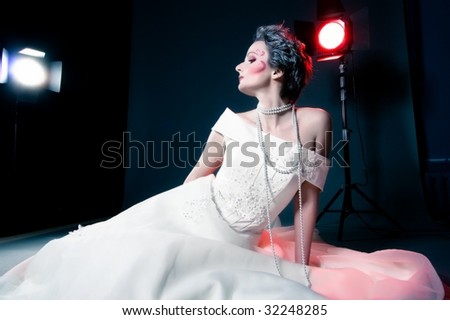 Slim beautiful woman with silver hair wearing luxurious wedding dress over dark studio background and lights