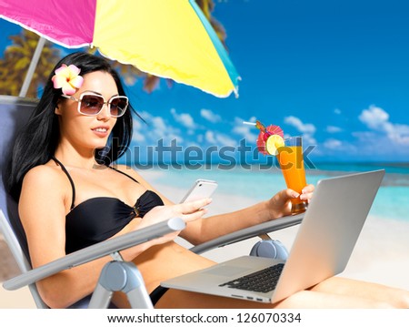 Young woman on the beach with a laptop and mobile phone sending message. Vacation and communication concept.
