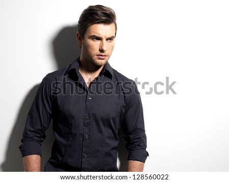 Fashion portrait of young man in black shirt poses over wall with contrast shadows