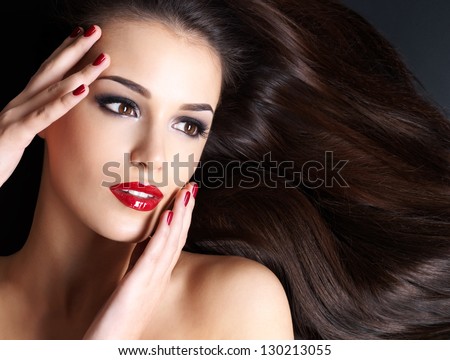 Beautiful woman with long brown straight hairs and red nails lying on the dark background