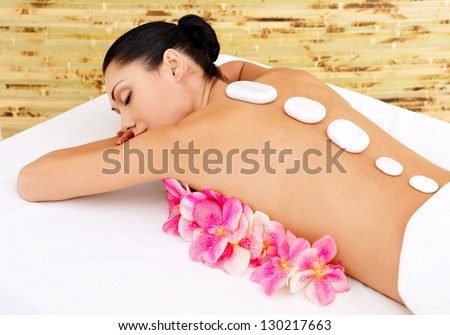 Body care for young woman at beauty spa salon. White hot stones on female back.