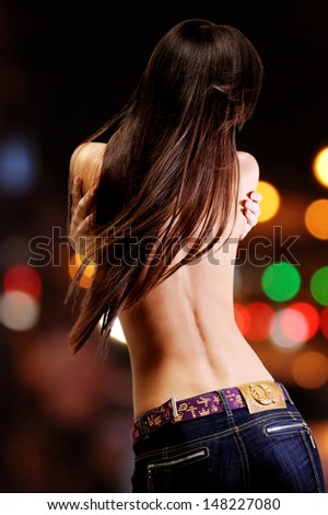 rear view of young attractive woman with long brown hair over bright night lights