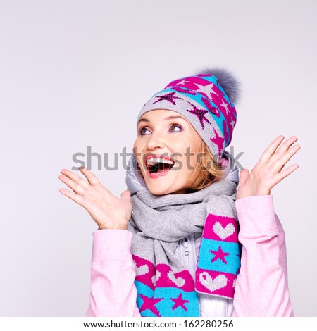 Photo of a happy surprised woman in winter clothes with bright positive emotions looking up - at studio