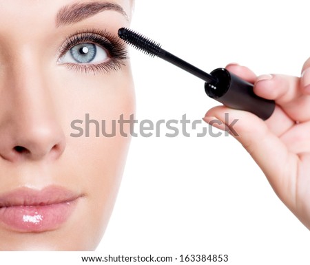 Young white woman applying mascara on eyelashes  - macro shot over white background