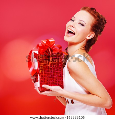Happy laughing woman with birthday present in hands posing over red background