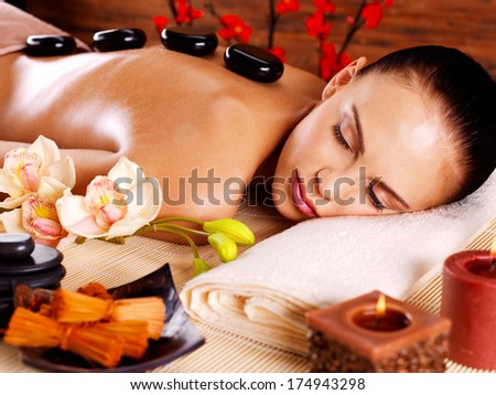 Adult woman relaxing in spa salon with hot stones on back. Beauty treatment therapy