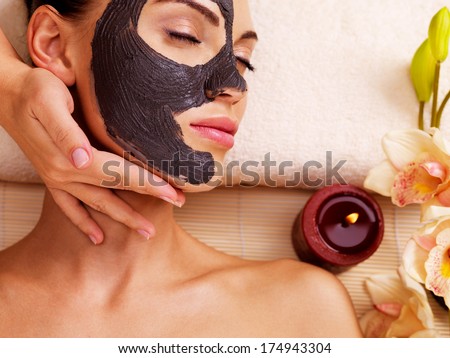 Cosmetologist doing massage on the woman\'s face  in sap salon. Female with scrub cosmetic mask on face.