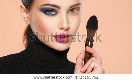 Portrait of a girl with cosmetic brush near face. Woman making makeup on the face using makeup brush. One half face of a beautiful white woman with  bright makeup and the other is natural. 