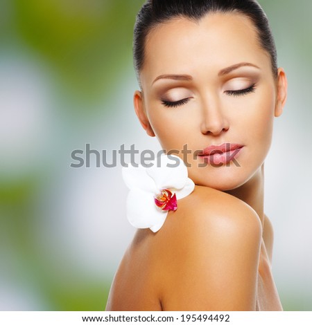 Beauty face of  beautiful woman with a white orchid flower. Skin care treatment. Green nature background