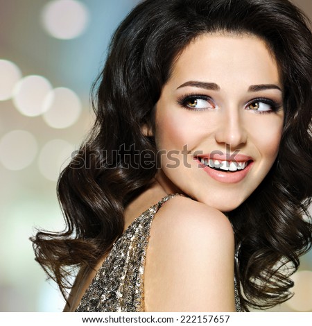 Portrait of the beautiful young happy laughing woman with brown curly hairs looking away. Pretty fashion model with dark eye makeup