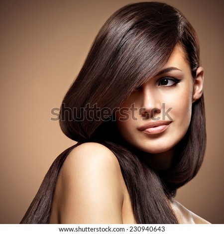 Beautiful young woman with long straight brown hair. Fashion model posing at studio over beige background