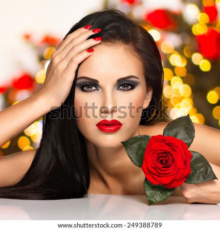 Portrait of a beautiful young woman with red lips,  nails and rose flower in hand. Fashion model with black eye makeup posing at studio over night lights balls. Soft bokeh background concept.
