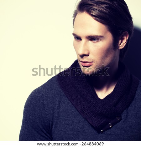 Handsome sexy man in gray pullover poses over wall with contrast shadows and looking sideways.