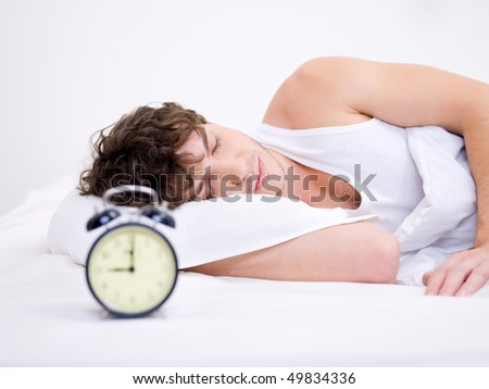 The young man sleeping with alarm clock near his head