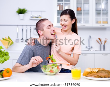 Happy playful young couple eating together in the kitchen
