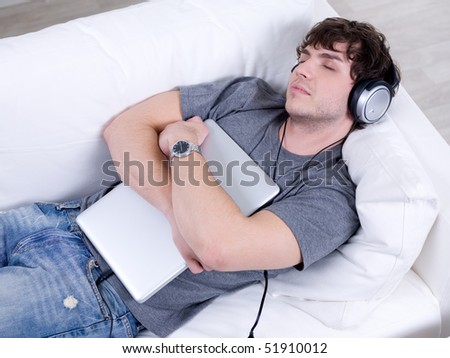 Man listening music in headphone and sleeping in embrace with laptop on the sofa
