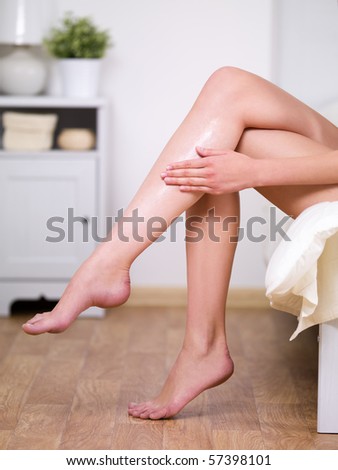Beautiful fresh legs of young woman applying cream on it - indoors