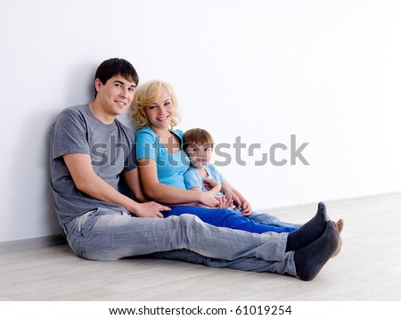 Happy family in casuals with little son sitting on the floor in empty room - indoors