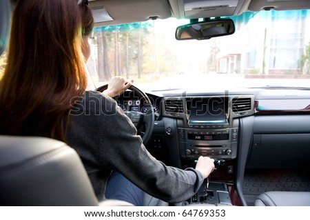 The young woman driving  the car. View from back seats of the car.